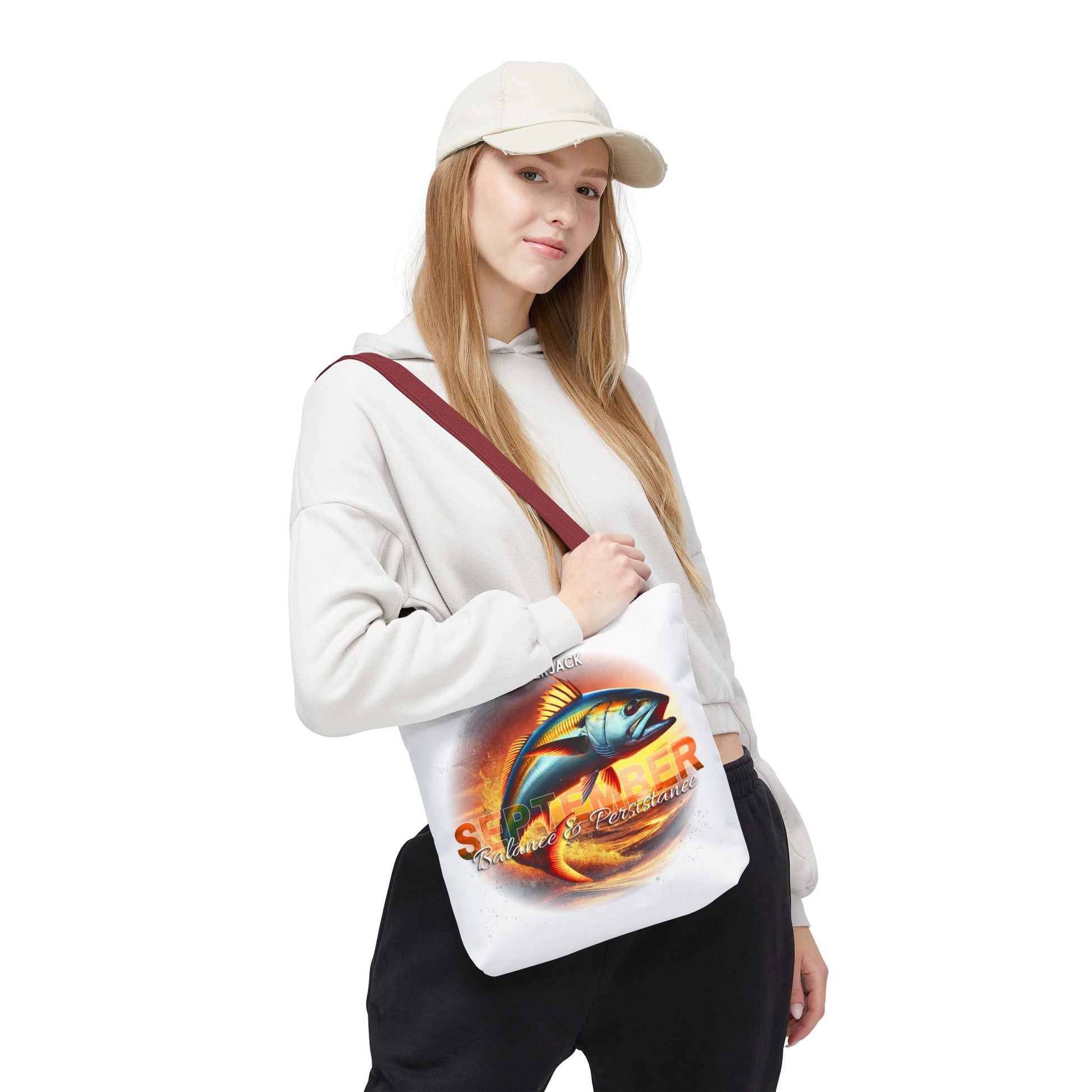 Woman wearing beige cap and hoodie holding a birth month beach tote with colorful fish design