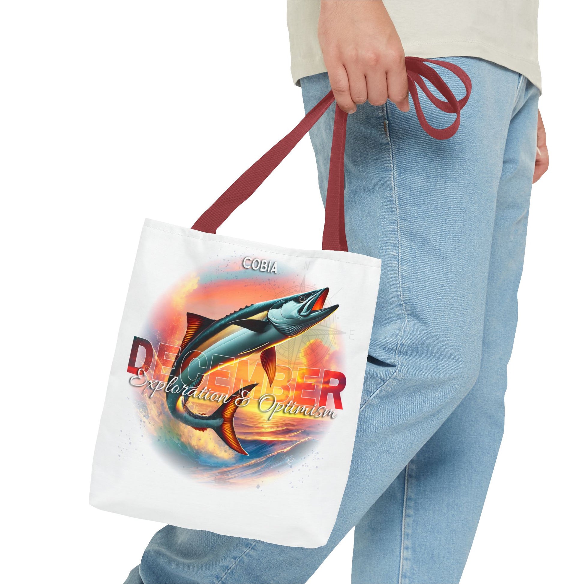 Birth month beach tote with colorful fish design and red handles held by person in jeans