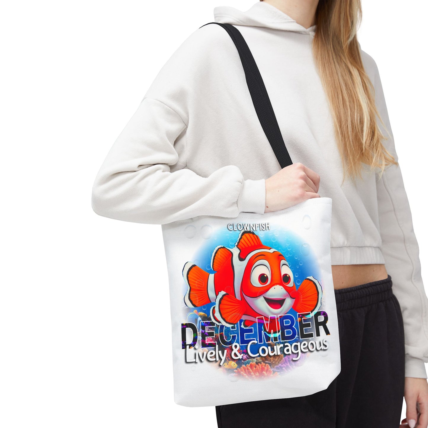 Kids birth month beach tote bag with colorful clownfish and December text worn by woman in white hoodie