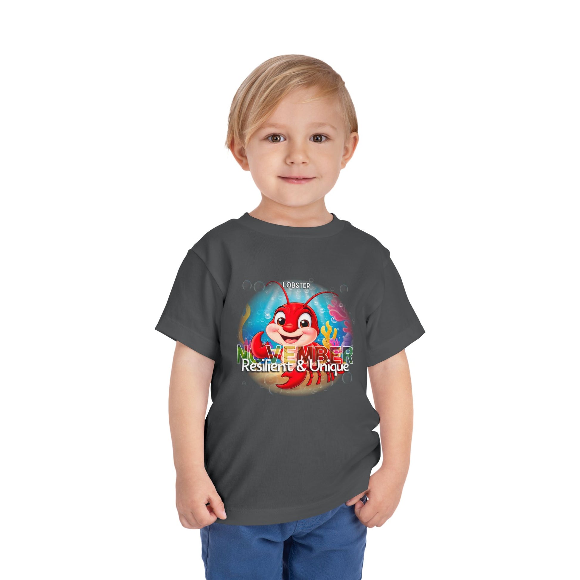 Toddler wearing a kids birth month tshirt featuring a November lobster design with resilient and unique text