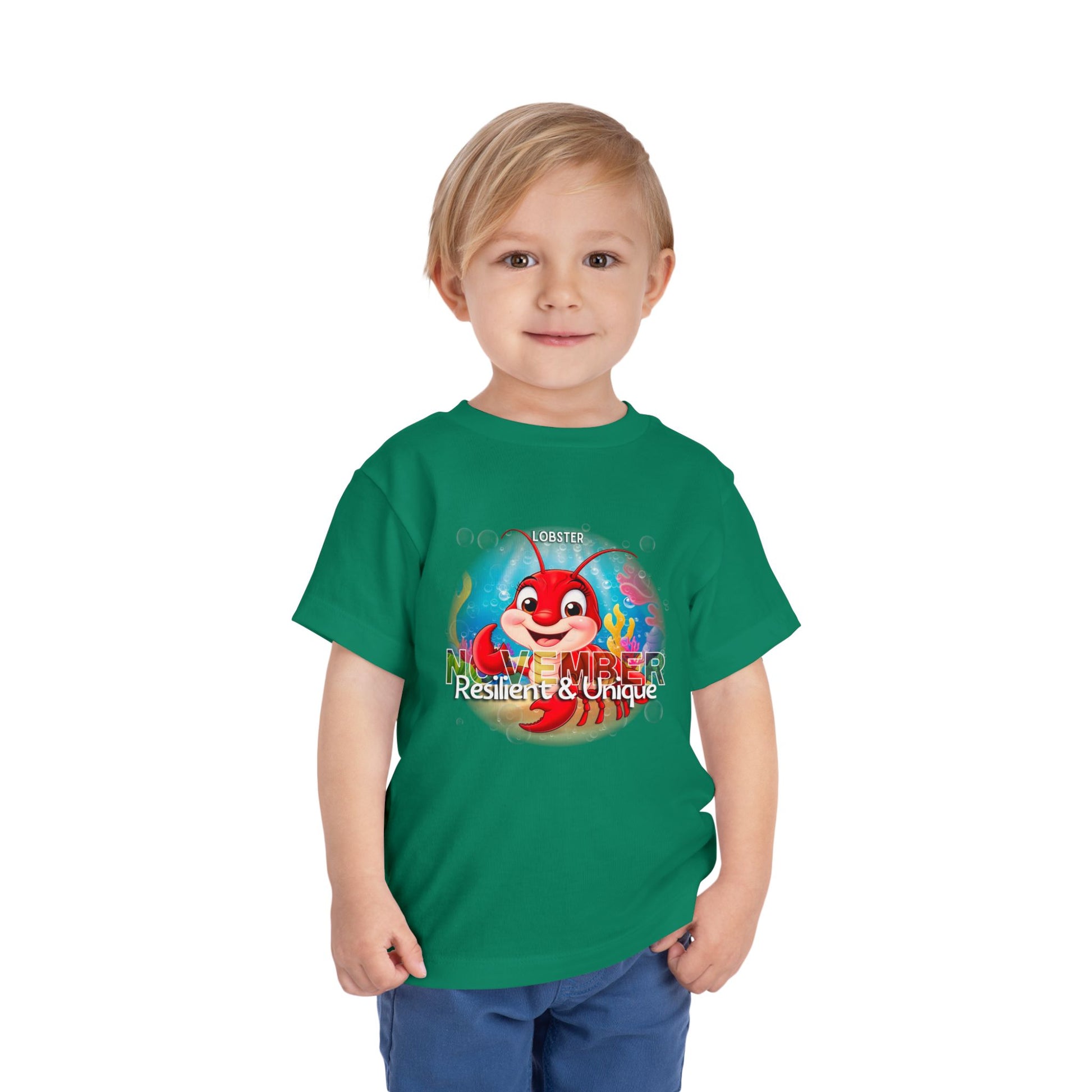 Green kids birth month tshirt featuring a red lobster cartoon and November text worn by a smiling toddler
