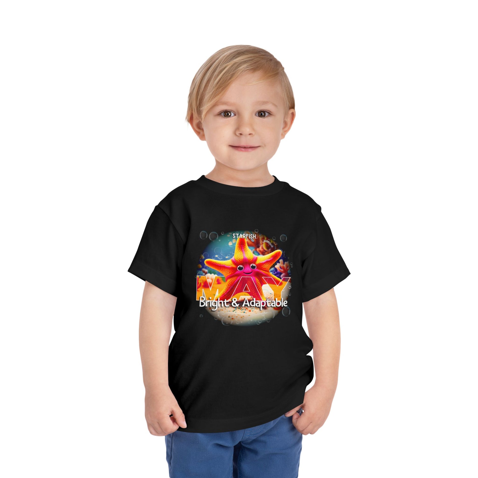 Toddler wearing a black kids birth month tshirt with a colorful starfish design and text bright and adaptable