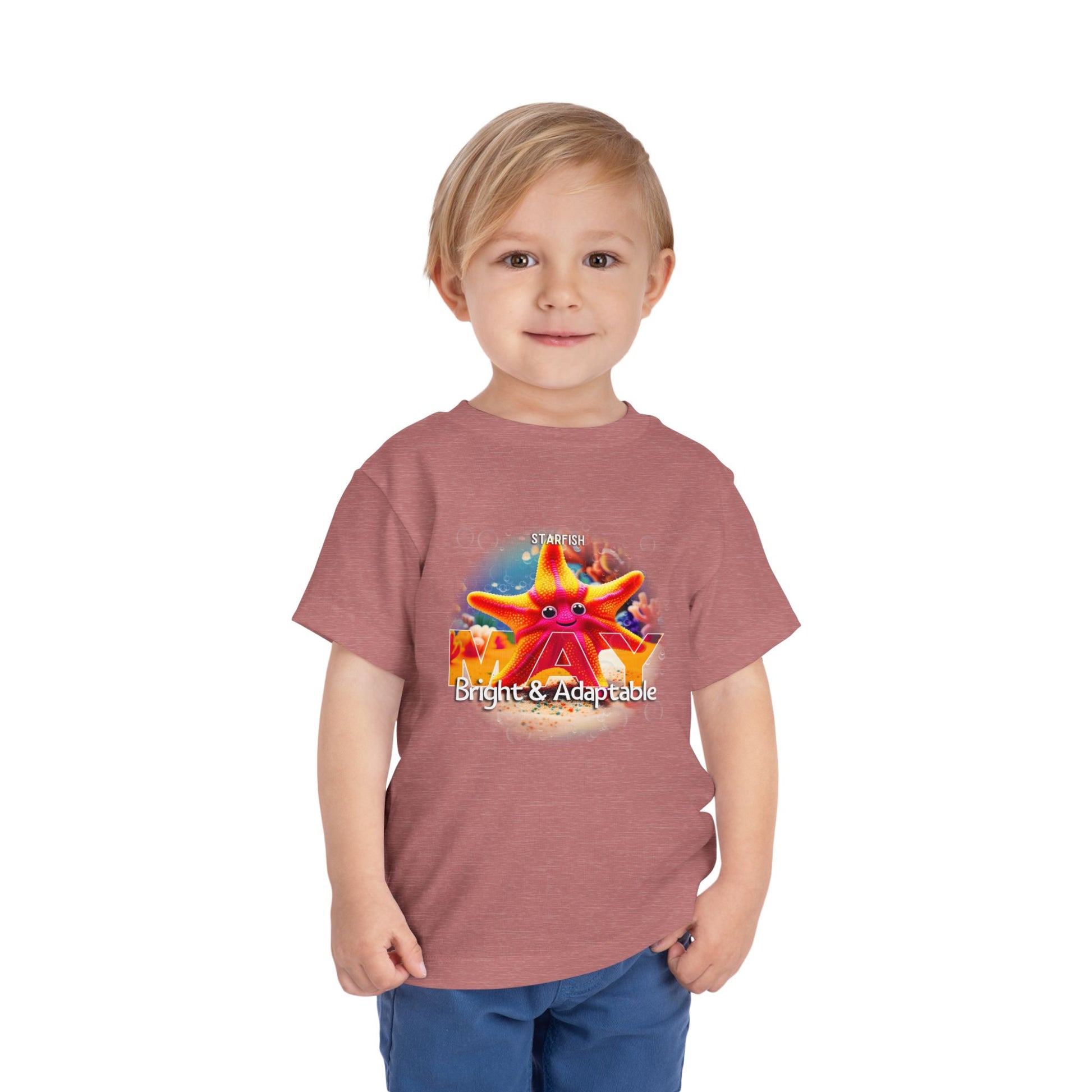 Little boy wearing a kids birth month tshirt with a colorful starfish design and text Bright Adaptable
