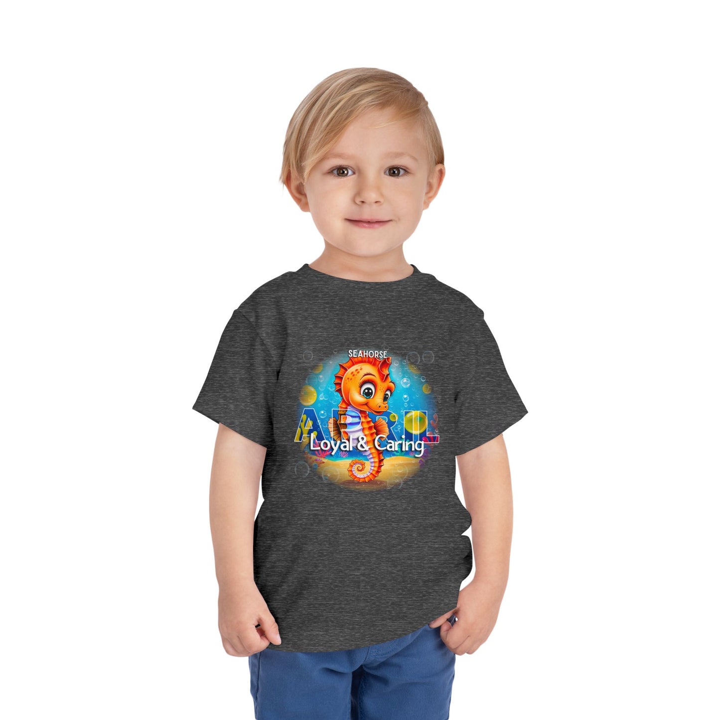 Toddler wearing a dark gray kids birth month tshirt featuring a colorful seahorse design with Loyal and Caring text