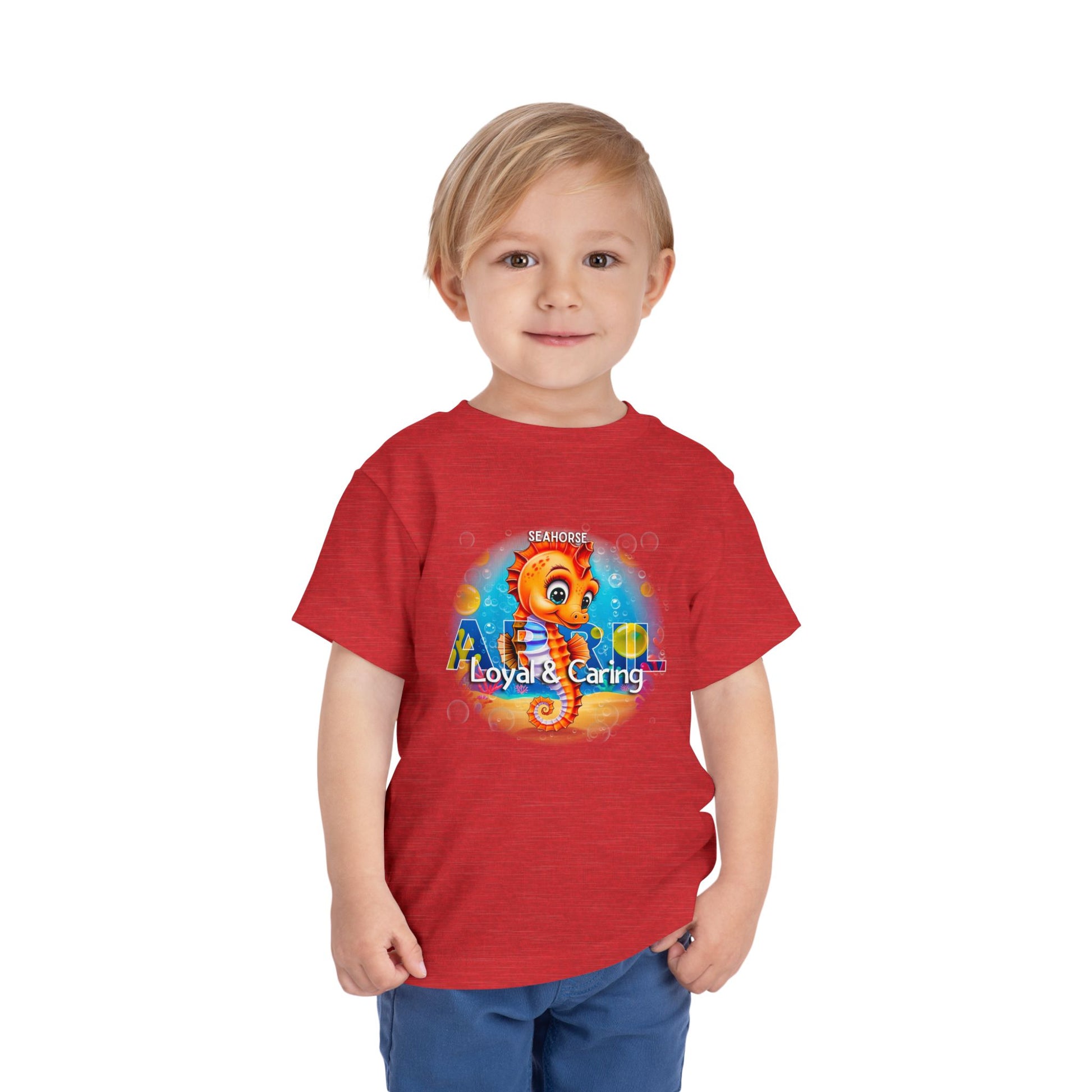 Toddler wearing red kids birth month tshirt featuring a colorful seahorse design with loyal and caring text
