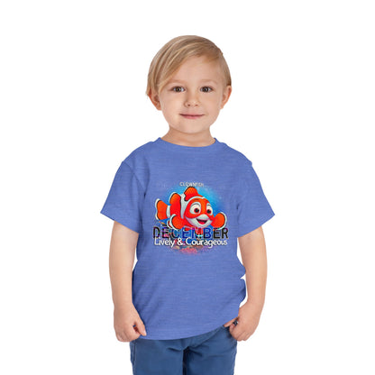 Toddler wearing a blue kids birth month tshirt with December clownfish design and lively courageous text