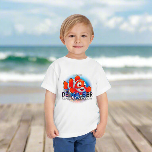 Young boy wearing a white kids birth month tshirt with December and cartoon fish design at the beach