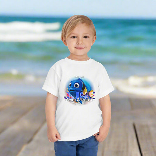 Toddler wearing a kids birth month tshirt featuring a playful animated fish design on a beach background